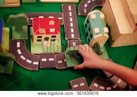 Top View Of A Kid Building A City From Wooden Blocks With Trees, Roads And Buildings.