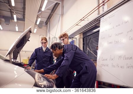 Male Tutor With Students Looking At Car Engine On Auto Mechanic Apprenticeship Course At College