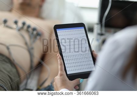 Close-up Of Female Cardiologist Holding Tablet And Examine Patients Heartbeat. Person Laying On Hosp
