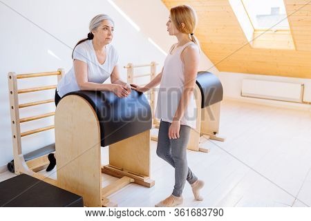 Young Professional Instructor Helping An Elderly Woman Cant Workout Independently Doing Stretching B
