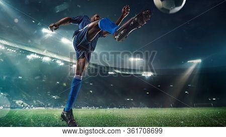 Professional Football Or Soccer Player In Action On Stadium With Flashlights, Kicking Ball For Winni