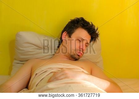 Portrait Of Sleeping Man In Bed At Home In Poor Flat Lying In Reclining Pose. He Is Breathing Deep. 