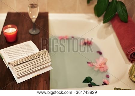 Bath With Flower Petals. Book, Candles And Glass Of Wine On A Wood Tray. Organic Spa Relaxation In C