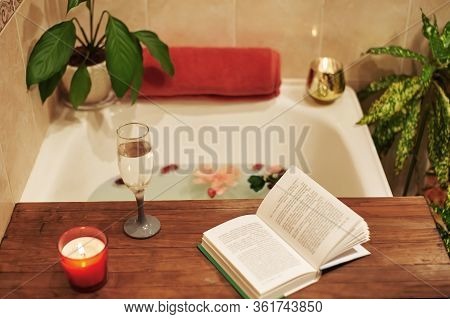 Bath With Flower Petals. Book, Candles And Glass Of Wine On A Wood Tray. Organic Spa Relaxation In C