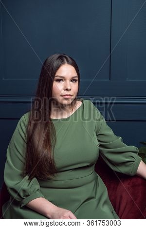 Pretty Young Lady In A Evening Dress Sitting In A Chair On Dark Blue Background. Plus Size Caucasian