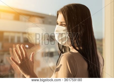 Young woman with veil looking at window, home isolation concept. Covid-19 pandemic situation in self isolation at home. New corona virus changes normal lives.