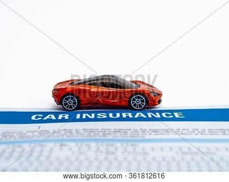 High Angle Close Up Shot Of An Orange Sports Car Toy With Insurance Paper On White Background