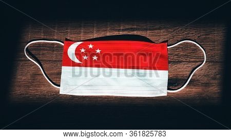 Singapore National Flag At Medical, Surgical, Protection Mask On Black Wooden Background. Coronaviru
