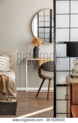 Elegant Round Mirror In Wooden Frame Above Fancy Console Table With Flowers In Vase In Trendy Bedroo