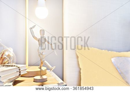 Wooden Dummy Doll Posing And Dancing In The Blurred Bedroom Background With A Flashing Lamp And Book