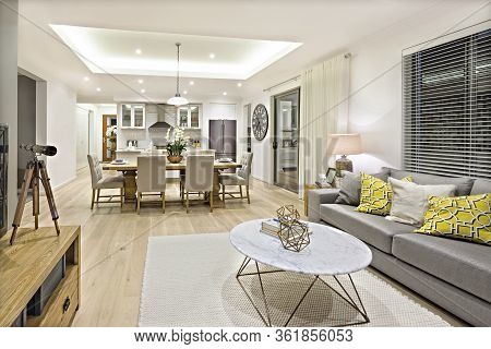 Modern Living Room Including Sofas, Chairs And Tables Beside The Kitchen And Dining Room Illuminated