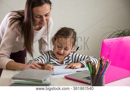 Adult Woman Helping Ethnic Girl To Do Homework Assignment In Notebook Near Laptop During Studies At 