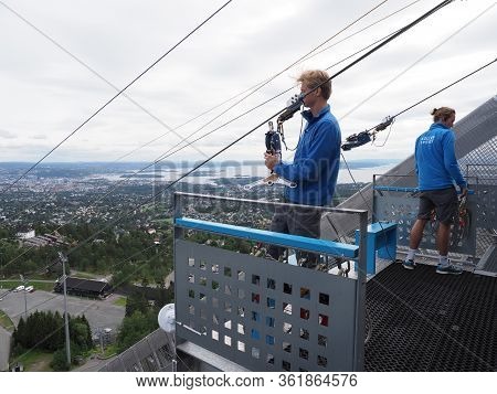 Oslo, Norway On July 2019: Two Men Care About Zipline Rider In European City Seen From Ski Jump In H