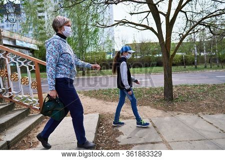 woman and child girl walks down the street during the day, a pedestrian walkway and buildings with apartments, a residential area, a medical mask on their faces protects against viruses and dust