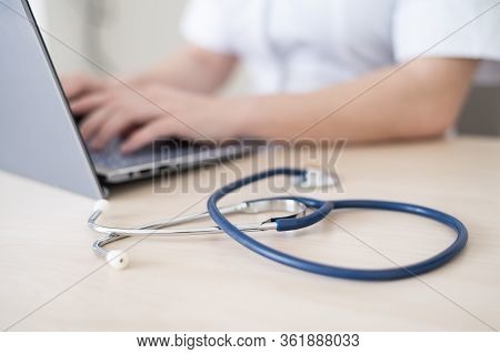 Unrecognizable Female Doctor In Uniform Uses A Laptop. Faceless Medical Worker Writes A Report On Th