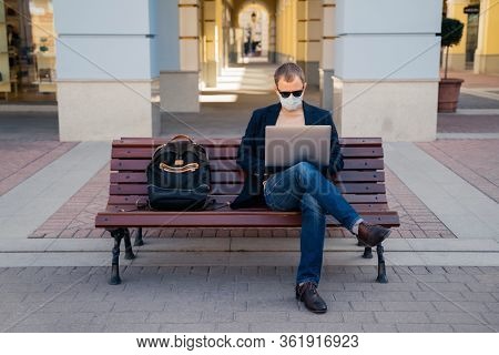 Photo Of Busy Man Freelancer In Mask Does Distance Work, Keyborads On Laptop Computer, Sits At Woode