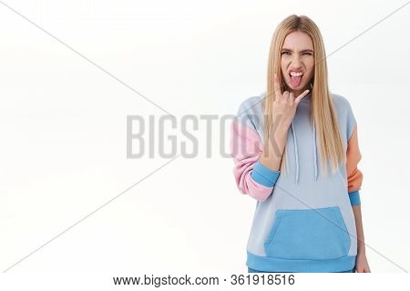 Rebellious And Daring, Good-looking Blonde Girl In Hoodie, Showing Tongue And Rock-n-roll Sign As Ha