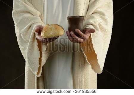 Jesus holding and offering the bread and a cup of wine against a dark background