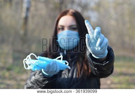 Young Woman In Protective Mask Shows Sanitizer Spray Bottles And Protective Face Masks Outdoors In S