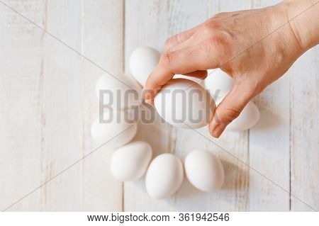 A White Chicken Egg Lying In A Man’s Hand, Shot On A White Painted Wooden Surface. Background For Li