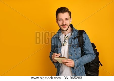Young Journalist With Glasses Over His Collar,in A White T-shirt And Denim Jacket Over Yellow Backgr