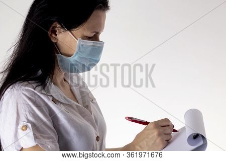 A Masked Nurse Is Writing On A Tablet. Threat Of The Pandemic Coronavirus Covid-19.