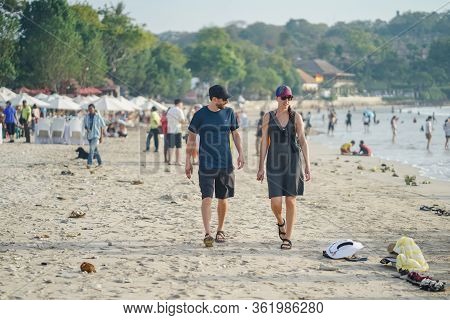 Bali, Indonesia - December 2019: A Pair Of Tourist Is Walking On Jimbaran Beach Before Sunset. This 
