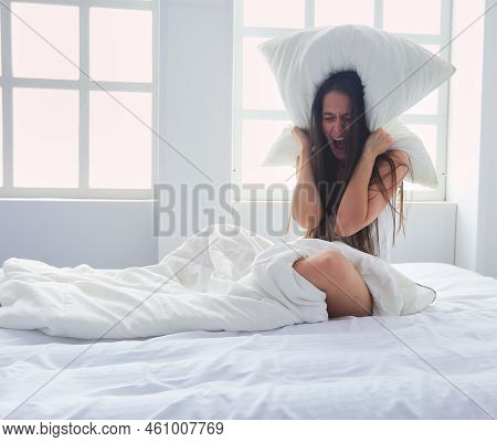 Young Caucasian Woman Covering Her Head And Ears With Pillows.