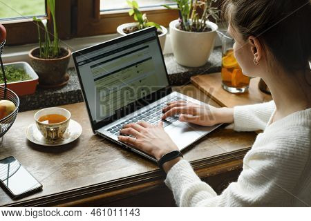 Young Freelancer Working On Laptop At Home. Woman Using Computer On The Kitchen For Work. Distant Jo