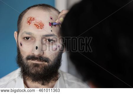 Artist Using Makeup And Costume To Create Zombie Look, Sitting In Studio. Man Waiting To Look Dramat