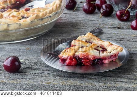 A Slice Of Freshly Baked Cherry Pie With The Full Pie In Soft Focus In Behind.