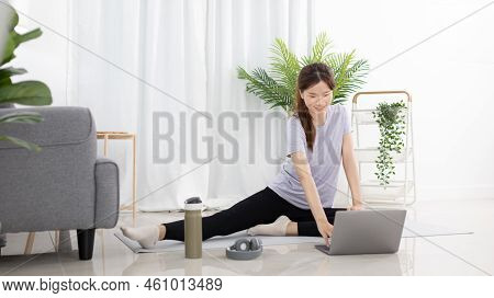 Beautiful Asian woman watching yoga teacher and light exercises in her living room at home, Watch li
