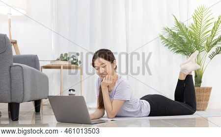 Beautiful Asian woman watching yoga teacher and light exercises in her living room at home, Watch li