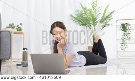 Beautiful Asian woman watching yoga teacher and light exercises in her living room at home, Watch li