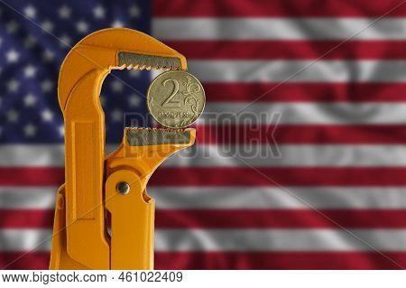 Russian Two Rubles Coin Held In An Orange Plumber Wrench On The Background Of The Flag Of The United