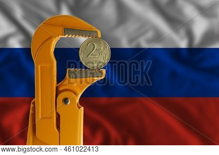 Russian Two Rubles Coin Held In An Orange Plumber Wrench On The Background Of The Russian Flag. Reve
