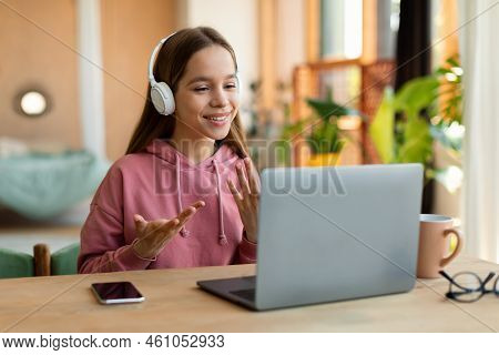 Positive Schoolgirl Having Video Call With Tutor, Talking To Laptop Webcamera, Sitting At Desk At Ho