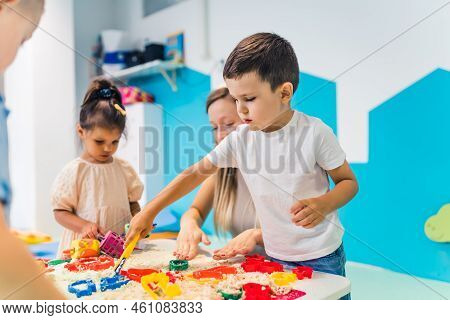 Fun Sensory Play With Moldable Kinetic Sand At Nursery School. Toddlers Standing Around The Table An