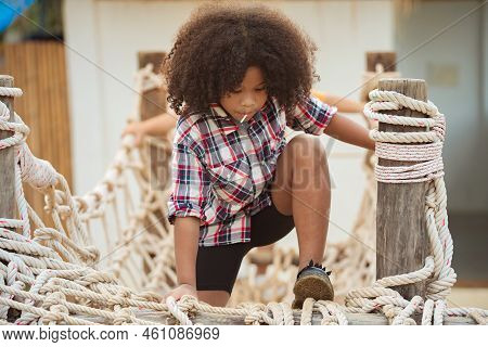 African American Kid Girl Playing On A Rope-ladder Web In A Playground.