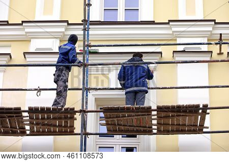 Workers Repair The Building Wall Standing On Scaffolding. Builders Painting The Facade, Construction
