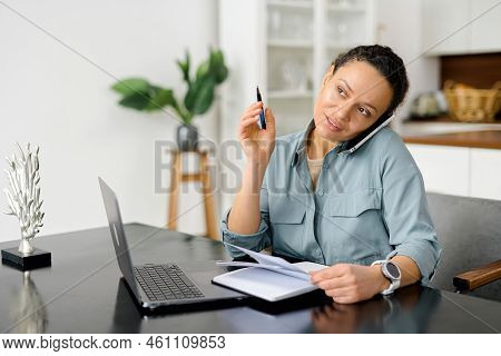 Freelance Woman Talks On The Smartphone And Takes Notes With Pen, Using Laptop For Remote Work From 