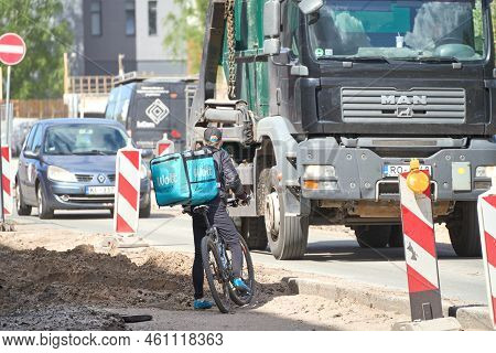 Riga, Latvia - May 13, 2022. A Cyclist From Wolt Food Delivery Company Trying To Cross Road Under Re