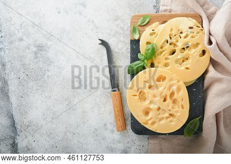 Cheese Maasdam Or Radamer. Piece Of Cheese On Black Marble Or Stone Standa On Old Grey Concrete Back