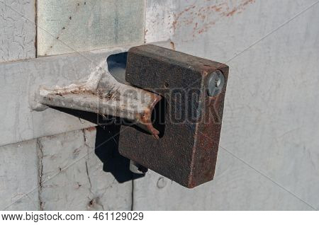 A Padlock Hangs On Old Metal Garage Or Warehouse Doors. Daylight