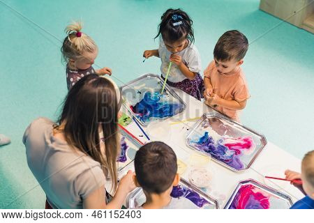 Multicultural Group Of Children At The Nursery School Milk Painting, Using Pigments For Color. Finge