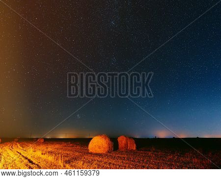 Night Starry Sky Above Rural Landscape Field Meadow With Rolls Of Straw In Fields After Harvest. Agr