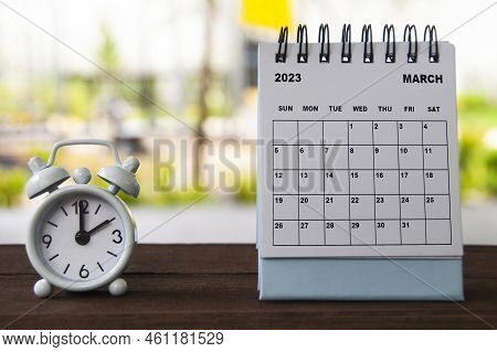 Alarm Clock Pointing At 2 O'clock With March Calendar On A Bench. Time And Calendar Concept.