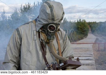 A Military Man In A Chemical Protection Suit And A Gas Mask Measures The Level Of Radiation On A Con