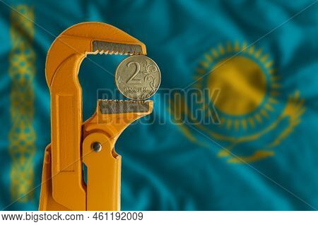 Russian Two Rubles Coin Held In An Orange Plumber Wrench On The Background Of The Flag Of Kazakhstan