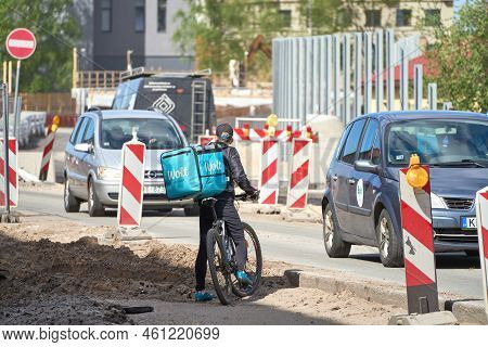 Riga, Latvia - May 13, 2022. A Cyclist From Wolt Food Delivery Company Trying To Cross Road Under Re